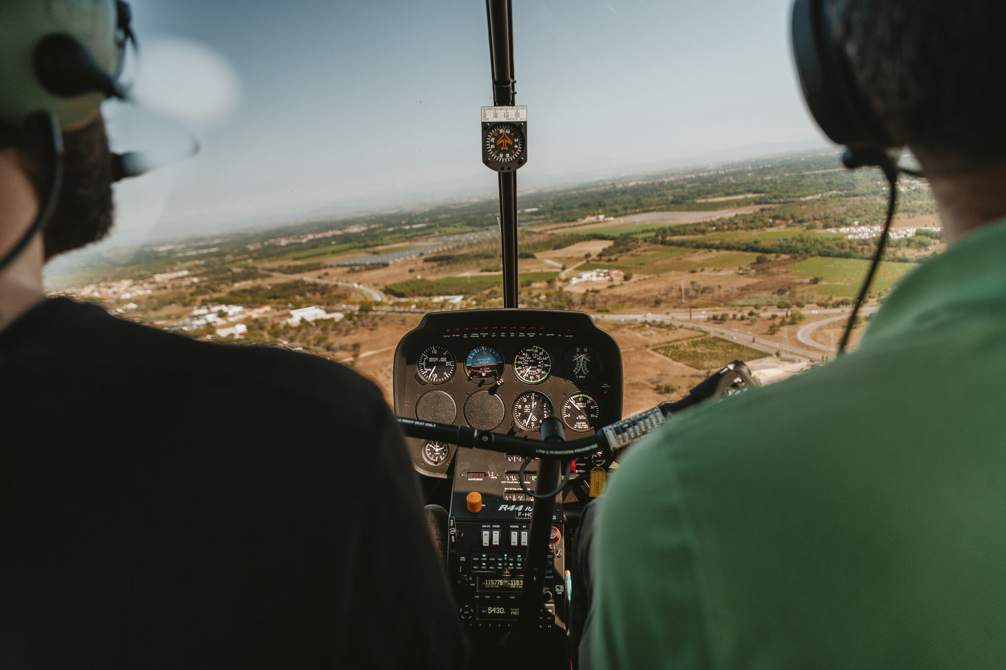 Vue du cockpit d'hélicoptère : deux personnes, paysage visible et instruments de vol.
